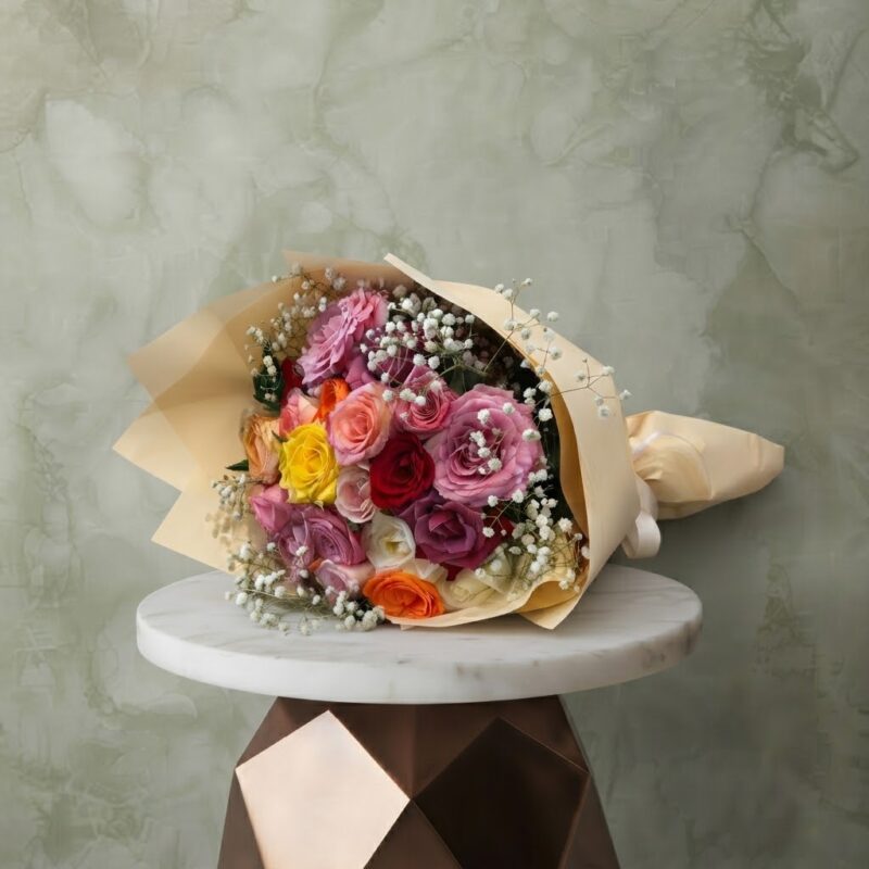 Mixed roses bouquet with colorful roses and white baby's breath wrapped in cream paper on a marble table.