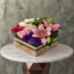 Luxurious flowers in a glass box with wooden base featuring pink lilies and purple flowers in Amman-زهور فاخرة في بوكس زجاجي محاط بإطار خشبي أنيق يتضمن ليليوم وردي وزهور بنفسجية في عمان.