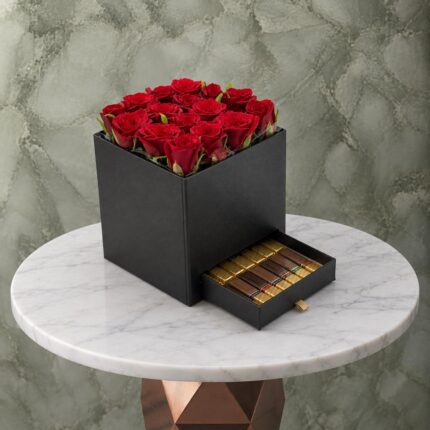 صندوق أسود فاخر يضم تنسيق ورد أحمر طبيعي مع درج يحتوي على شوكولاته فاخرة -Luxury black box featuring natural red roses arrangement with a pull