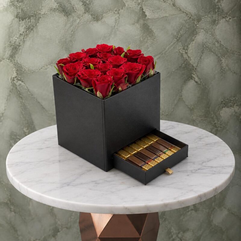 صندوق أسود فاخر يضم تنسيق ورد أحمر طبيعي مع درج يحتوي على شوكولاته فاخرة -Luxury black box featuring natural red roses arrangement with a pull