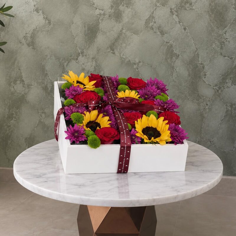 Floral masterpiece box in a white wooden box featuring sunflowers, red roses, and chrysanthemums in Amman-لوحة الأزهار الفاخرة في بوكس خشبي أبيض يحتوي على عباد الشمس والورد الأحمر والأقحوان في عمان.