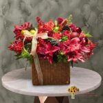 Luxury Christmas arrangement in a woven basket with red lilies, ornaments, and pinecones in Amman-تنسيق فاخر لعيد الميلاد في سلة قش مع ليليوم أحمر وكرات زينة وصنوبر في عمان.