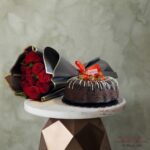 Red roses with chocolate cake topped with fresh strawberries and black luxury wrapping paper.