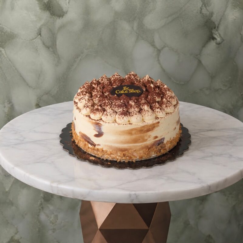An authentic italian tiramisu cake topped with cocoa powder and the Cake Shop logo in Amman.كيكة التيراميسو الإيطالية