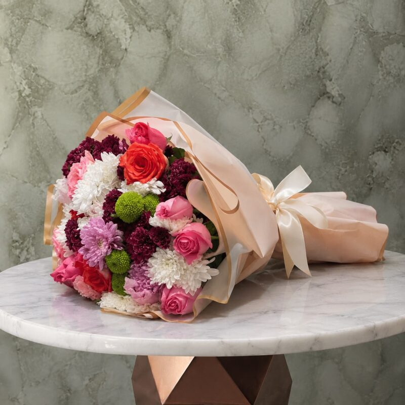 A colorful mixed flower bouquet with elegant pink wrapping and a satin bow in Amman-باقة ورود ملونة فاخرة بتغليف أنيق وعقدة ستان في عمان.