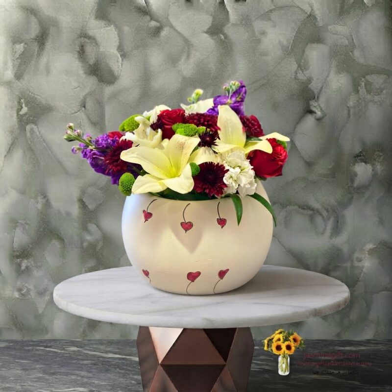White and red floral jar featuring diverse flower arrangements and lilies on a circular marble table.جرة الأناقة البيضاء والحمراء