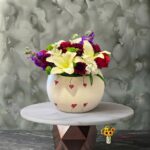 White and red floral jar featuring diverse flower arrangements and lilies on a circular marble table.جرة الأناقة البيضاء والحمراء