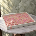 Baby girl chocolate tray amman featuring 100 pieces of pink customized newborn chocolates in a white tray.صينية شوكولاتة بنوتة بيبي في عمان