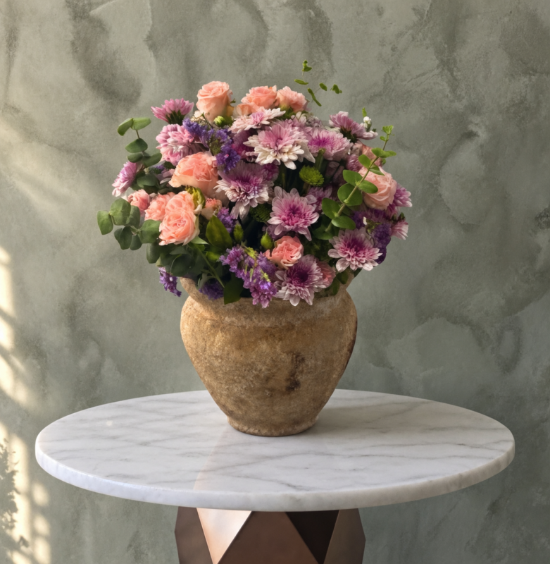 Royal purple bloom amman featuring purple and pink flowers in a rustic ceramic vase with eucalyptus.إشراقة البنفسج الملكي