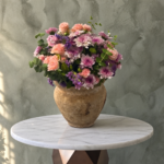 Royal purple bloom amman featuring purple and pink flowers in a rustic ceramic vase with eucalyptus.إشراقة البنفسج الملكي