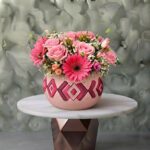 Handmade pink and floral jar amman featuring light pink roses, vibrant pink gerberas, and baby's breath in a patterned ceramic pot.
