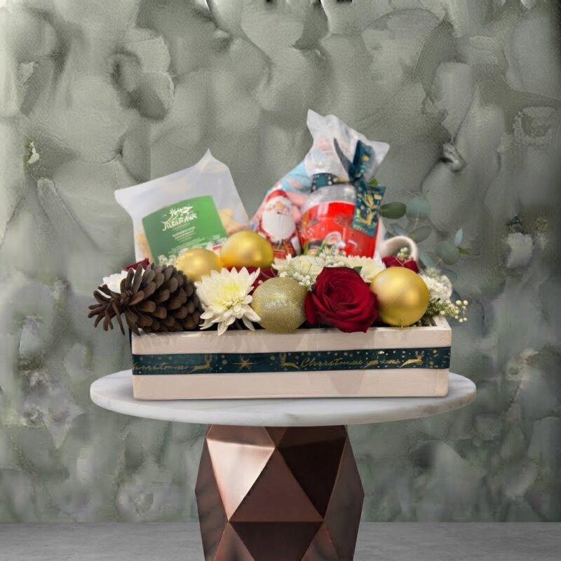 Festive joy christmas hamper amman featuring red roses, white chrysanthemums, pinecones, gold baubles, and holiday gifts in a wooden box.صندوق بهجة العيد