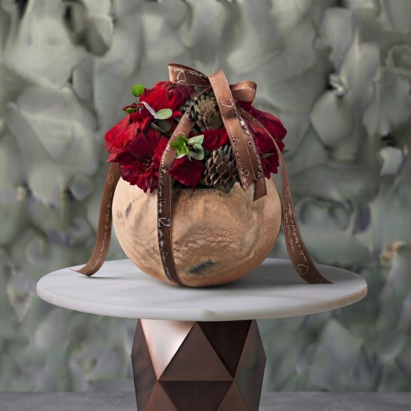 Rustic winter charm floral pot amman featuring vibrant red roses, dark chrysanthemums, and pinecones in a round pottery bowl tied with a printed ribbon.