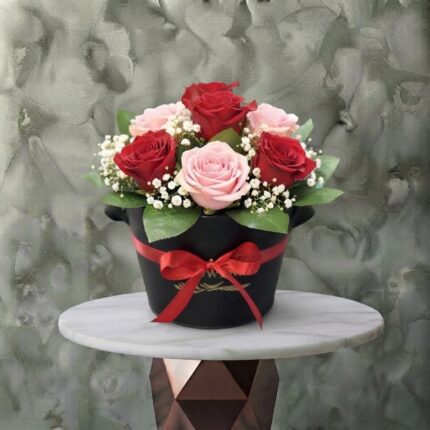 Beauty love amman arrangement featuring fresh red and soft pink roses, baby's breath, and greenery in a black box with a red ribbon bow.