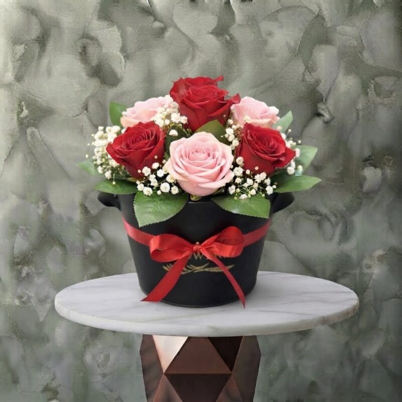 Beauty love amman arrangement featuring fresh red and soft pink roses, baby's breath, and greenery in a black box with a red ribbon bow.