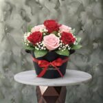 Beauty love amman arrangement featuring fresh red and soft pink roses, baby's breath, and greenery in a black box with a red ribbon bow.