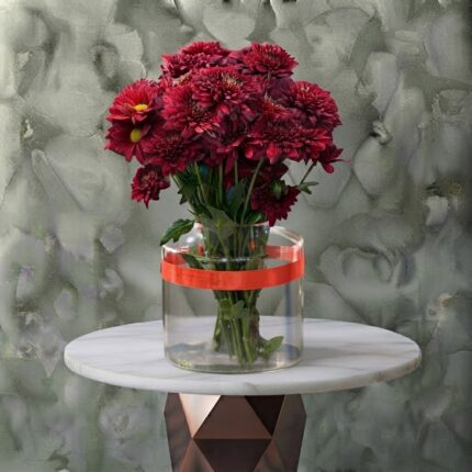 Golden heart bloom amman arrangement featuring rich dark red chrysanthemums and greenery in a cylindrical glass vase tied with a red ribbon.