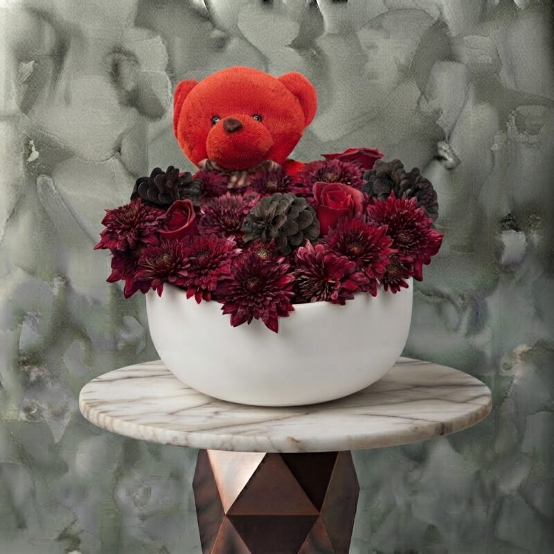 Velvet romance amman arrangement featuring a red teddy bear, rich dark chrysanthemums, roses, and pinecones in a modern white ceramic pot.
