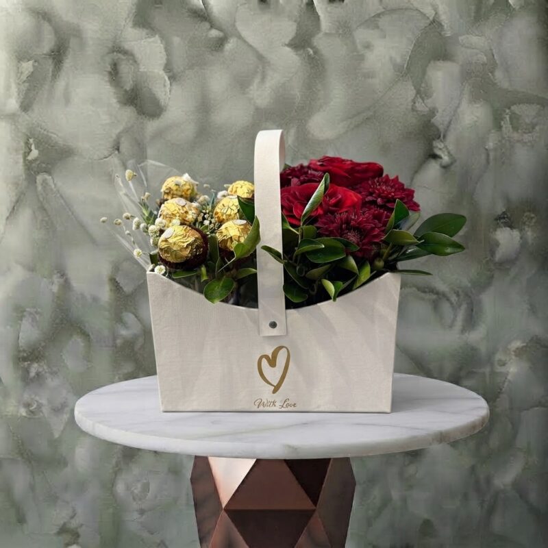 Charm box amman gift basket featuring red roses, baby's breath, and gold-wrapped chocolates in a white tote with center handle.بوكس الجمال