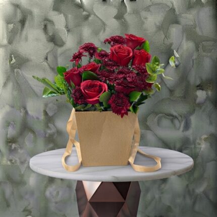 Crimson rustic amman arrangement featuring deep red roses and burgundy blooms with foliage inside a craft paper handle bag.ريف أحمر