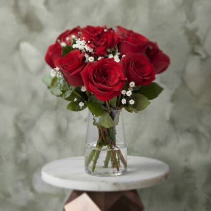 Red allure amman arrangement featuring classic red roses, white baby's breath, and greenery in a tall clear glass vase. - سحر الجوري