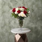 Rose radiance amman arrangement featuring red roses, white chrysanthemums, and baby's breath in a crystal clear glass vase.إشراقة الروز