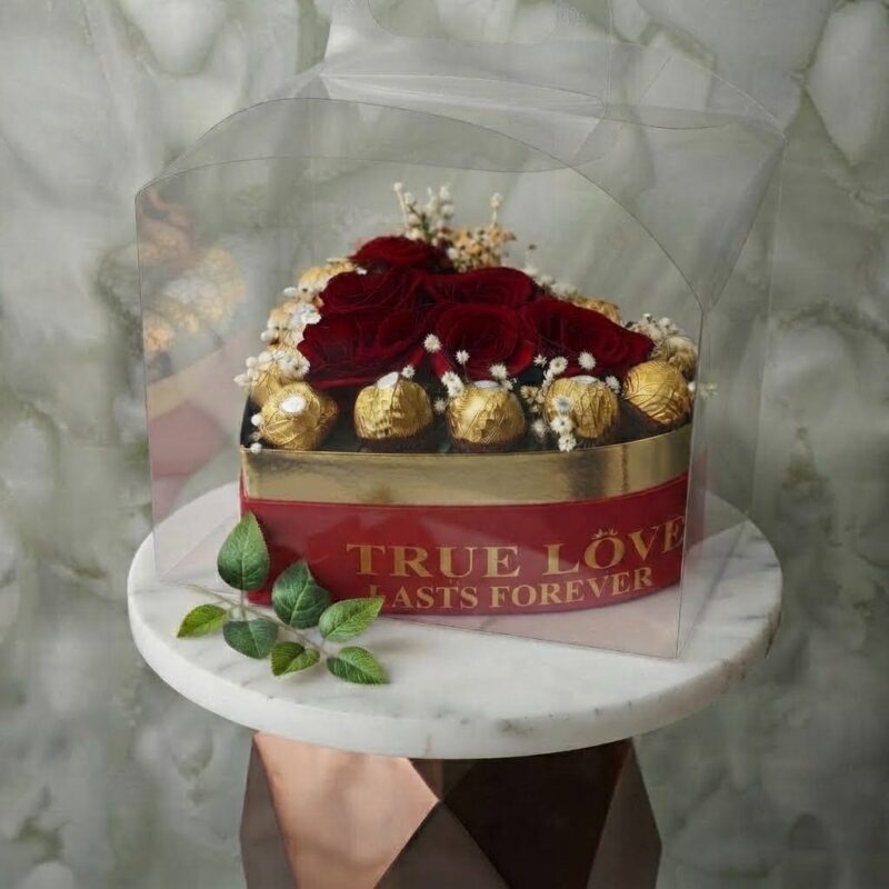 True love heart amman arrangement featuring red roses and golden-wrapped chocolates in a heart-shaped gift box with clear cover. قلب الحب الحقيقي