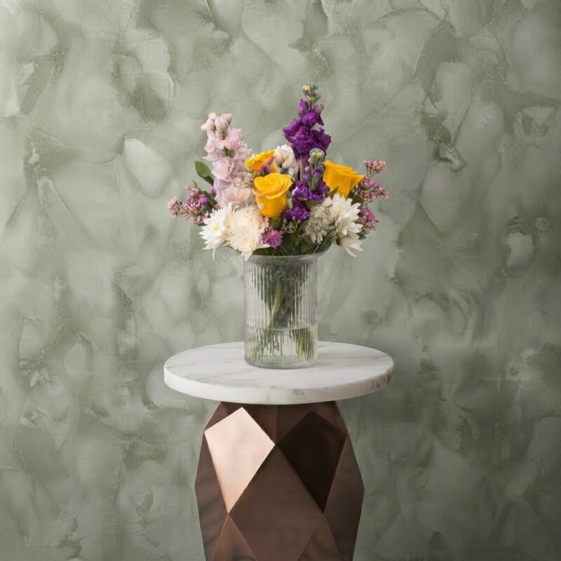 Bright hope vase amman with yellow roses, purple stock flowers, and white chrysanthemums in a clear ribbed glass vase.