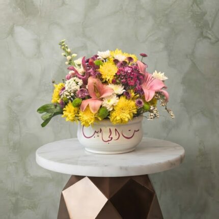 Sitt Al Habayeb amman floral arrangement with pink lilies and yellow flowers in a white ceramic bowl with Arabic calligraphy.