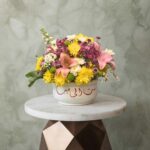 Sitt Al Habayeb amman floral arrangement with pink lilies and yellow flowers in a white ceramic bowl with Arabic calligraphy.