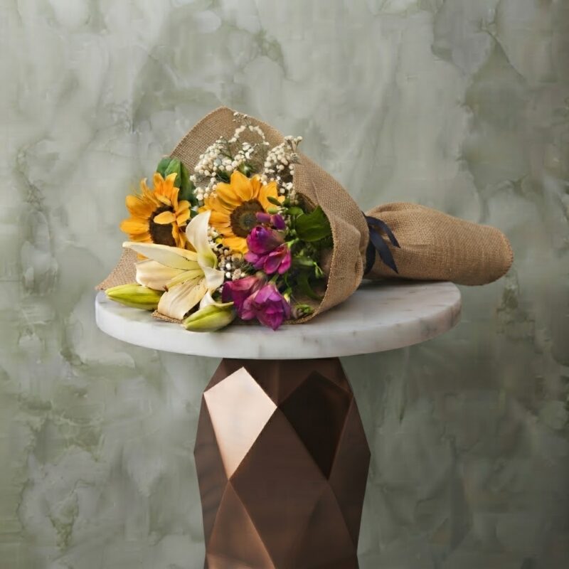 Small bouquet collection amman with sunflowers, white lilies, and rustic burlap paper on a marble table.