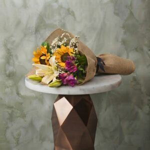 Small bouquet collection amman with sunflowers, white lilies, and rustic burlap paper on a marble table.