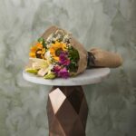 Small bouquet collection amman with sunflowers, white lilies, and rustic burlap paper on a marble table.