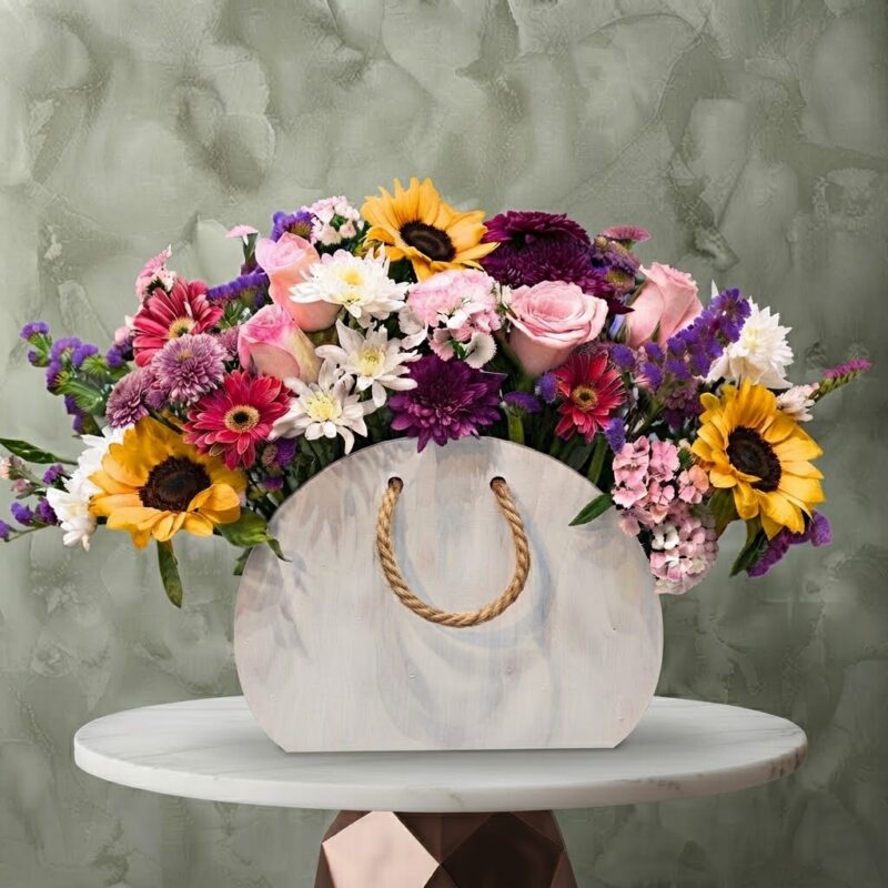 Spring sunrise bag amman floral arrangement with bright sunflowers, pink roses, and purple blooms in a wooden arched bag.