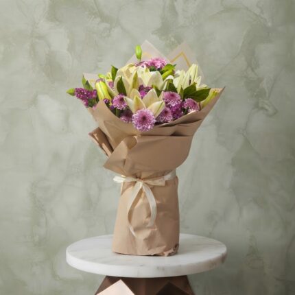 White lilies bouquet amman with purple chrysanthemums wrapped in brown kraft paper on a marble table.ليليوم أبيض و كريز نهدي زهري