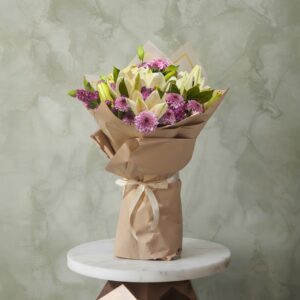 White lilies bouquet amman with purple chrysanthemums wrapped in brown kraft paper on a marble table.ليليوم أبيض و كريز نهدي زهري