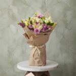 White lilies bouquet amman with purple chrysanthemums wrapped in brown kraft paper on a marble table.ليليوم أبيض و كريز نهدي زهري