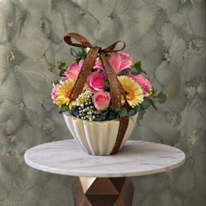 Blooming pink joy amman featuring pink roses and gerberas with a brown ribbon in a ceramic vase.