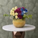 Harmonious color magic amman featuring white roses, purple chrysanthemums, and blue flowers in a textured vase.سحر الألوان المتناغمة