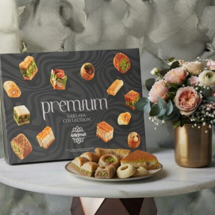 Alnejmah premium sweets collection featuring a baklava box and eastern desserts next to a vase of roses on a marble table.